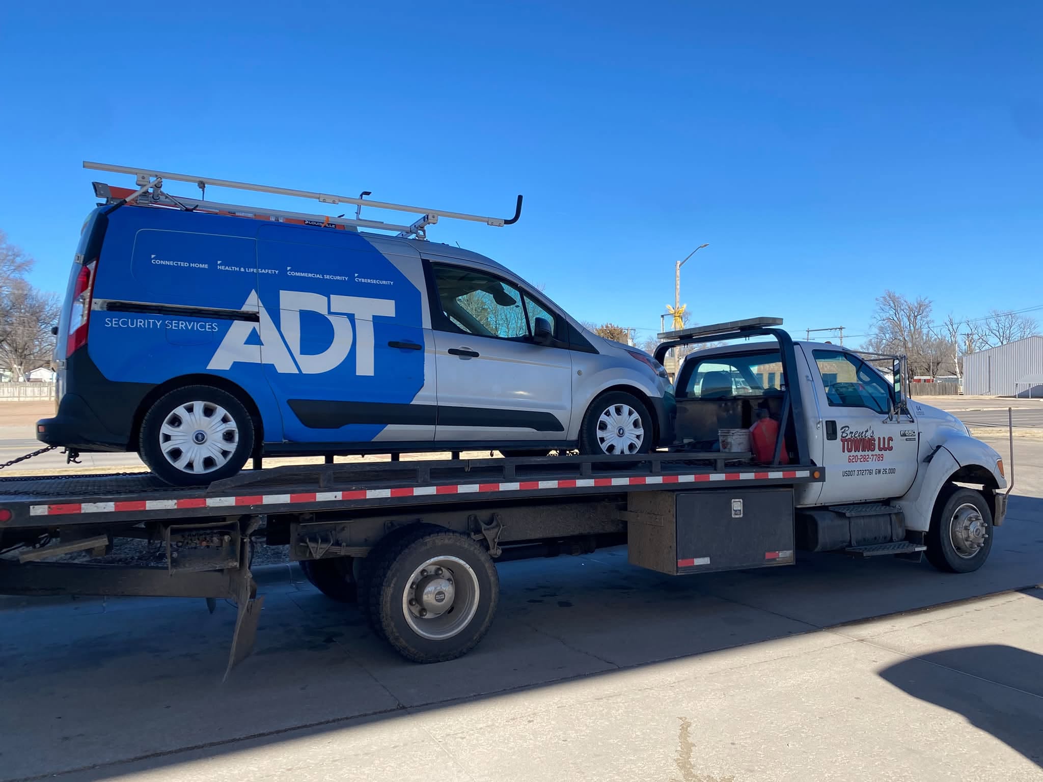 Flatbed tow truck hauling a branded ADT security services van